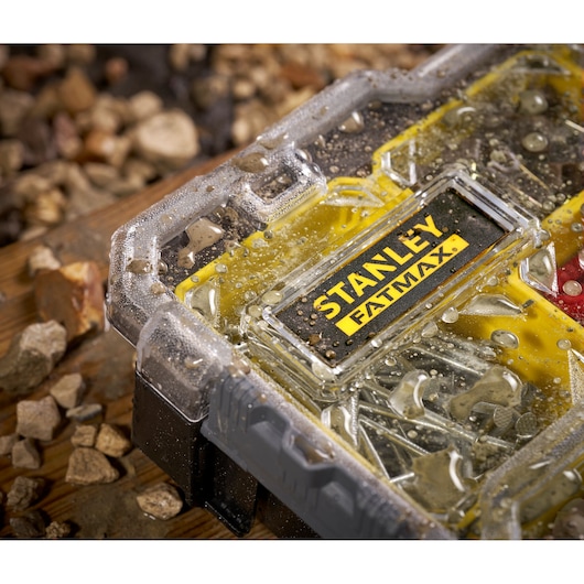 Photo of STANLEY FMST1-75781 waterproof small parts organizer with water droplets on clear lid, surrounded by rocks.