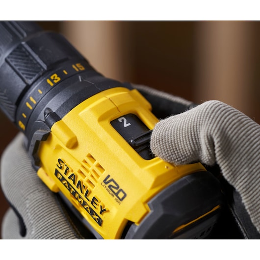 Close-up photo of STANLEY SFMCD710C2K cordless drill in use with gloved hand adjusting speed setting.