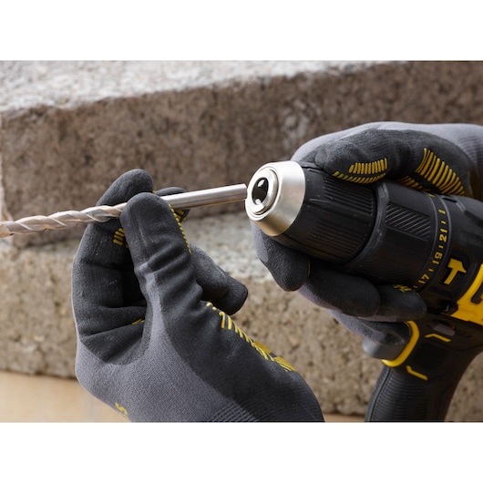 STANLEY SFMCD711C2K cordless drill close-up held in gloved hands, inserting a drill bit.