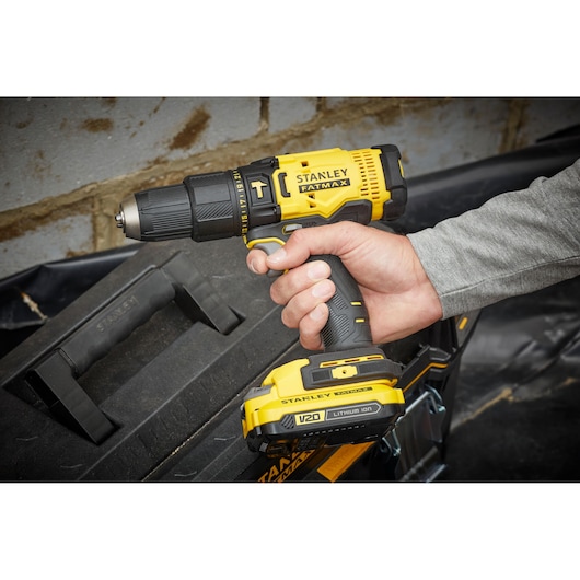 Stanley SFMCD711D22 cordless drill, yellow and black, FATMAX series, held in hand near toolbox.