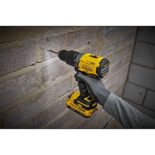 Photo of STANLEY SFMCD715C2K drill in use against a brick wall, yellow and black cordless power tool.