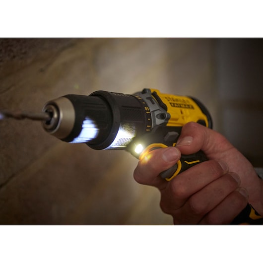 STANLEY SFMCD715C2K cordless drill with LED light, close-up drilling into wall, yellow and black body.