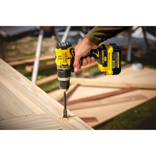 STANLEY SFMCD721M2K cordless drill in use, drilling into light wood outdoors, close-up view.