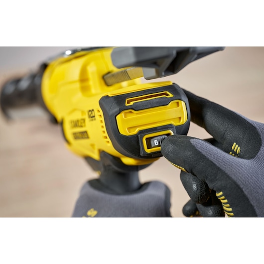 Photo of STANLEY SFMCE600B power tool, close-up of speed control dial being adjusted by gloved hand.