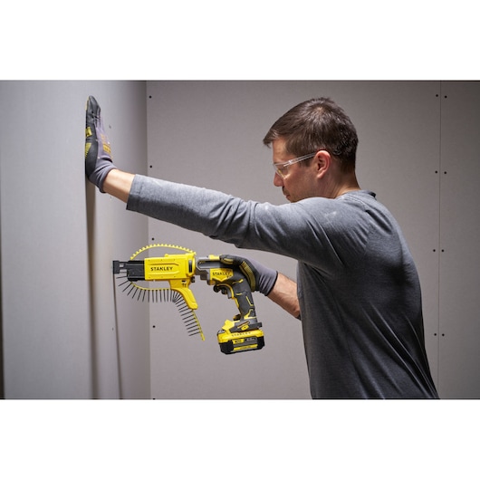 Person using STANLEY SFMCF600B cordless autofeed screwdriver with screw strip on drywall.