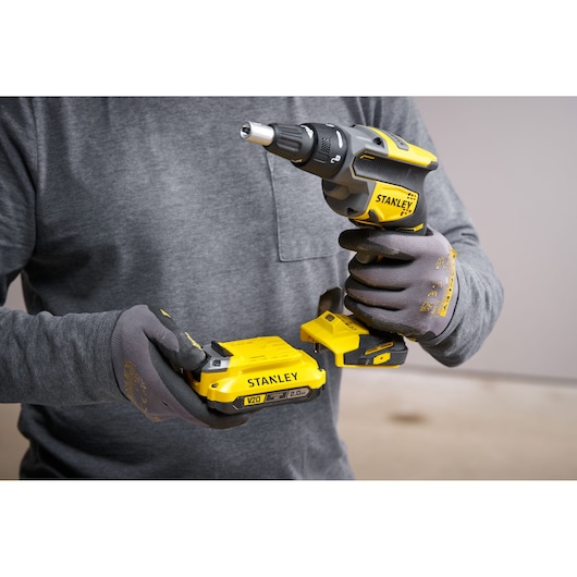 Photo of STANLEY SFMCF600B cordless screwdriver held by gloved hands, battery being attached.