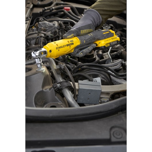 Photo of STANLEY SFMCF930B cordless ratchet tool being used on car engine by gloved hand.