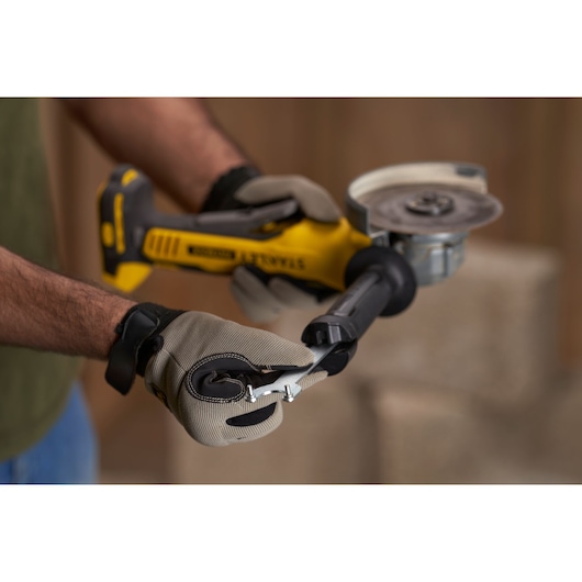 Stanley SFMCG700B cordless angle grinder held by gloved hands, close-up side view, photography product.