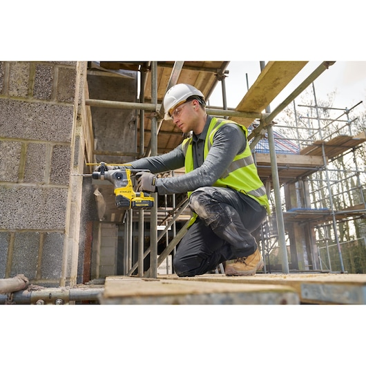 Photo of worker using STANLEY SFMCH910B rotary hammer drill on concrete wall at construction site.