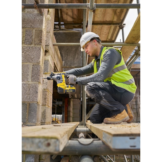 STANLEY SFMCH910B rotary hammer drill in use on a construction site, side view, operator drilling into concrete blocks.