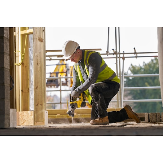 STANLEY SFMCH910B rotary hammer used by worker with hard hat and vest on construction site, front angle.