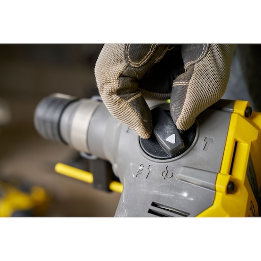 STANLEY SFMCH910B rotary hammer mode selector close-up, glove hand turning black dial, tool body yellow and grey.