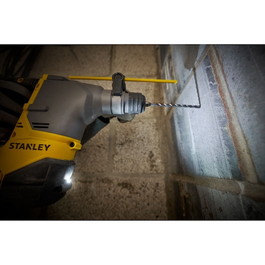 Photo of STANLEY SFMCH910B hammer drill in use drilling into a concrete wall, front close-up view.