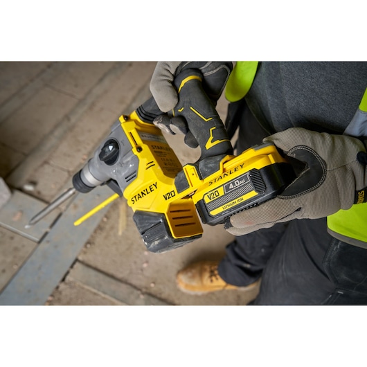 Photo of STANLEY SFMCH910B cordless rotary hammer in use on a construction site, yellow V20 battery visible.