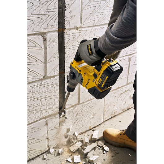 Photo of STANLEY SFMCH910M1T rotary hammer in use chiseling concrete wall, worker wearing gloves and boots.