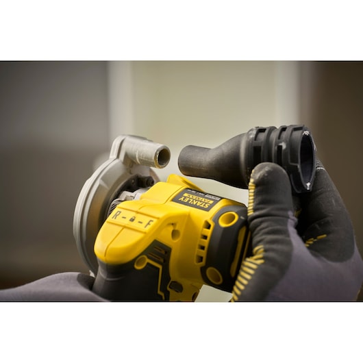 Close-up of STANLEY SFMCM300B angle grinder with yellow body, gloved hands attaching black accessory.