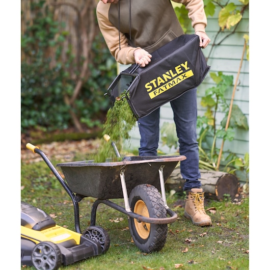 STANLEY SFMCMWS251B lawn mower grass bag being emptied into a wheelbarrow outdoors.