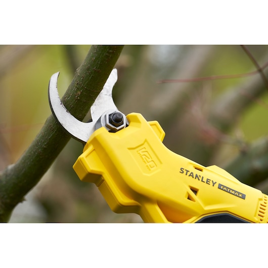 STANLEY SFMCPP32M1 yellow cordless pruning shear cutting tree branch, close-up photo outdoors.