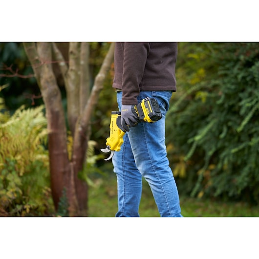 Photo of STANLEY SFMCPP32M1 cordless pruner held in hand, used outdoors in a garden setting.