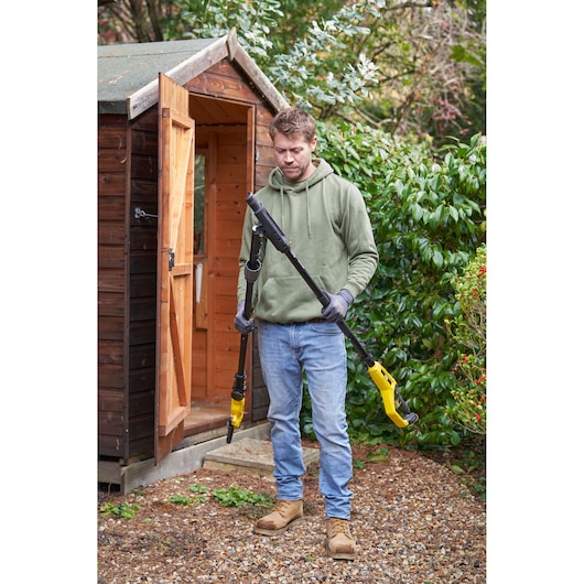STANLEY SFMCPP632D1 pole saw, yellow and black, outdoor view with person holding tool near wooden shed