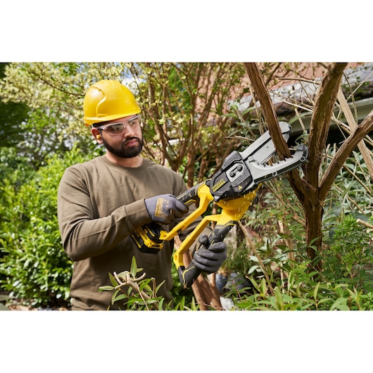Photo of worker using STANLEY SFMCPS515M1 cordless chainsaw to cut tree branches in garden.