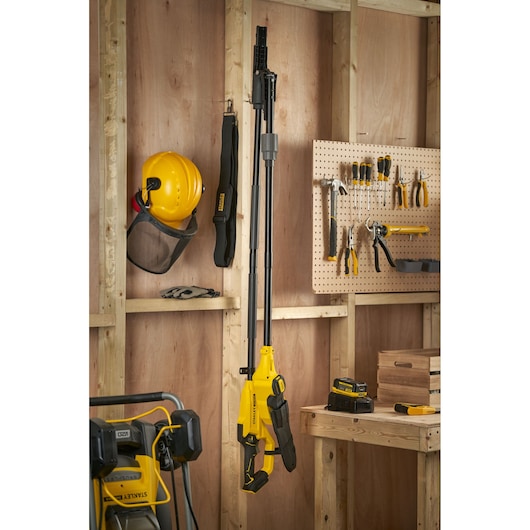 STANLEY SFMCPS720M1 pole saw hanging in workshop, yellow and black, surrounded by tools and safety gear.