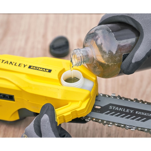 STANLEY SFMCPS720M1 chainsaw close-up, oil being poured into reservoir, yellow body and chain visible.