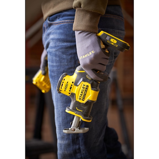 Photo of STANLEY SFMCS305B cordless reciprocating saw held by person wearing gloves, indoor workshop background.