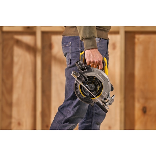 Photo of STANLEY SFMCS550B circular saw held by person, silver and black tool with yellow handle in workshop.