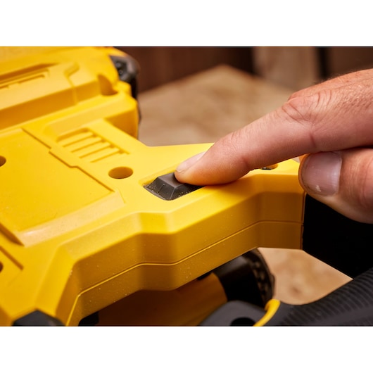 STANLEY SFMCS701M1 saw close-up, finger pressing black control button on yellow handle.