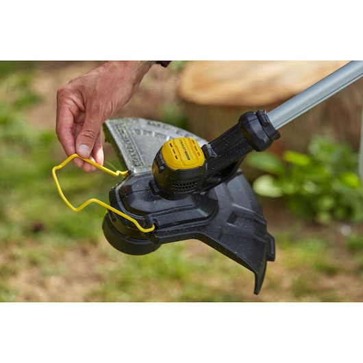 Photo of STANLEY SFMCST933M1 string trimmer head with yellow guard, close-up outdoors.