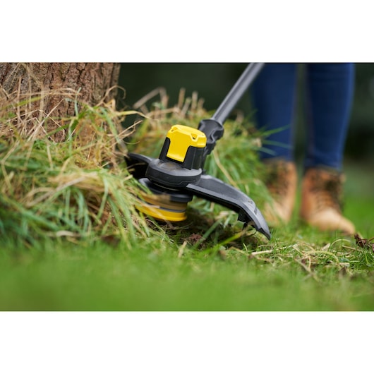 STANLEY SFMCSTB933M grass trimmer close-up cutting grass around tree, yellow and black design.