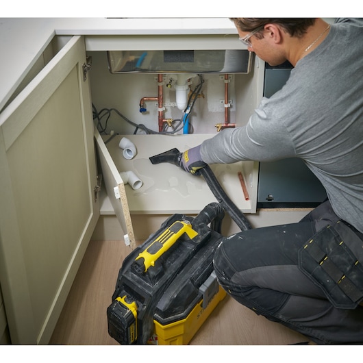 Person uses STANLEY wet/dry vacuum to clean water under sink during plumbing work.