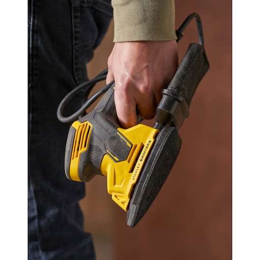 Photo of STANLEY SFMEW210S electric sander in hand, black and yellow design, product close-up.