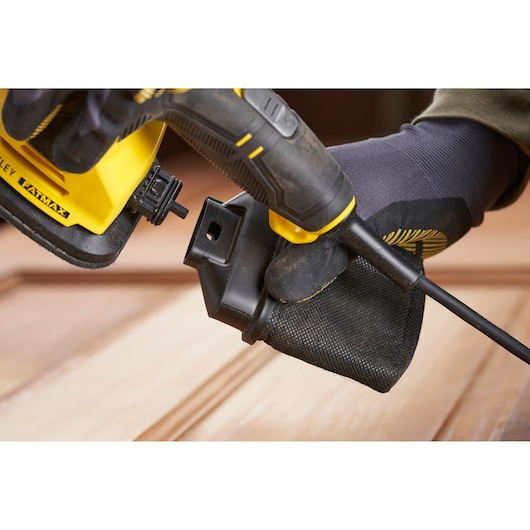Stanley SFMEW210S sander close-up, showing dust bag attachment, yellow and black tool in use.