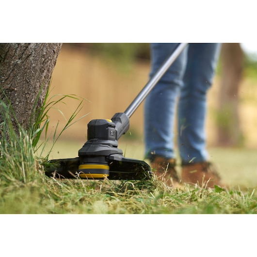 STANLEY SFMSTB930B grass trimmer close-up in use near a tree, trimming grass outdoors.