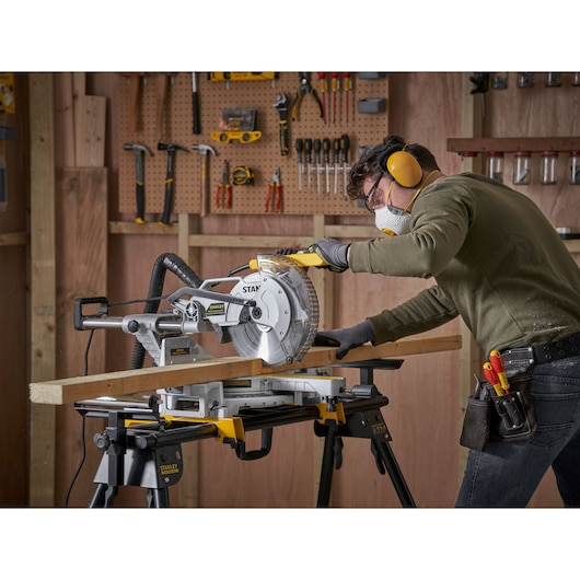 STANLEY SM1800 miter saw in use, cutting wood in workshop with tools on wall, side view.