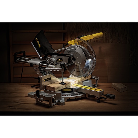 STANLEY SM1800 miter saw with laser guide, silver and yellow, shown cutting wood in workshop.