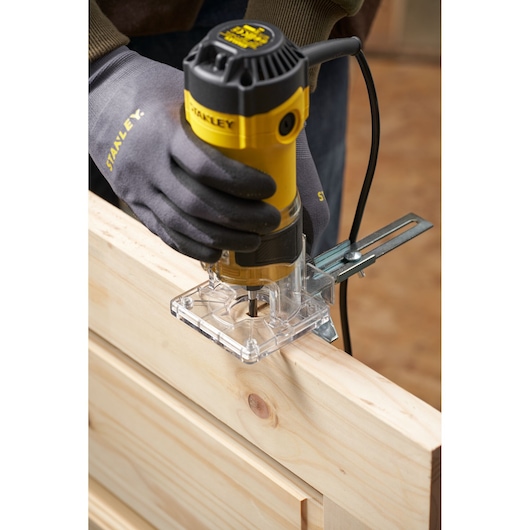 Photo of STANLEY ST55 trimmer used on wood edge, showing gloved hand holding the yellow power tool.