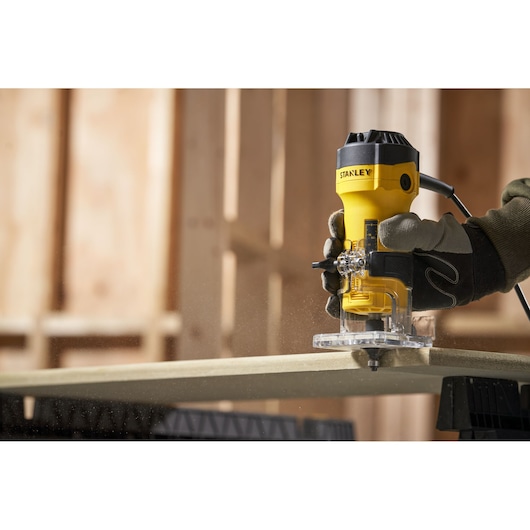 STANLEY ST55 compact router in use on wood with gloved hand, indoor workshop setting.