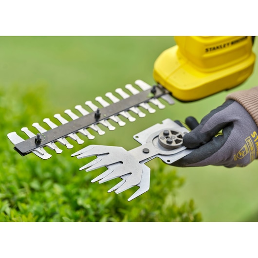 STANLEY STCSS20D1 hedge trimmer blade being changed, close-up outdoor photo with greenery background.