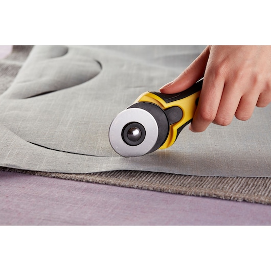 STANLEY STHT0-10194 rotary cutter tool held cutting gray fabric close-up.