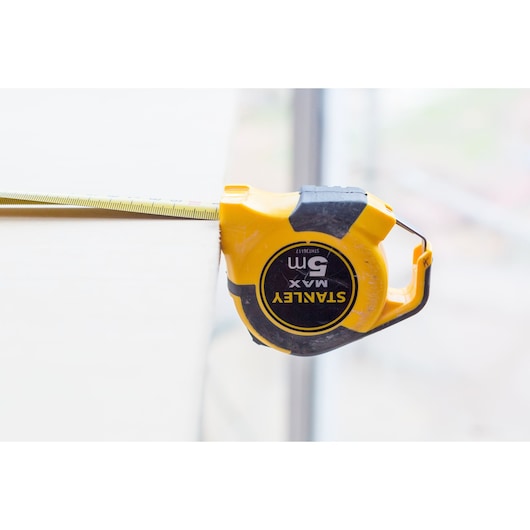 STANLEY STHT0-36117 tape measure, yellow and black, extended on a white surface, side angle.