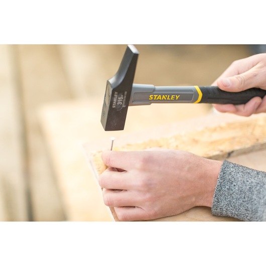 STANLEY STHT0-54159 hammer used to drive a nail into wood, close-up photography of hand tool in action.