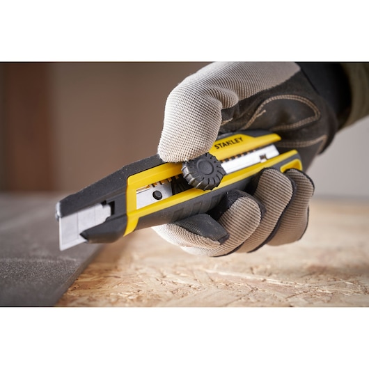 STANLEY STHT10500-0 utility knife, yellow and black, being used by a gloved hand to cut material.