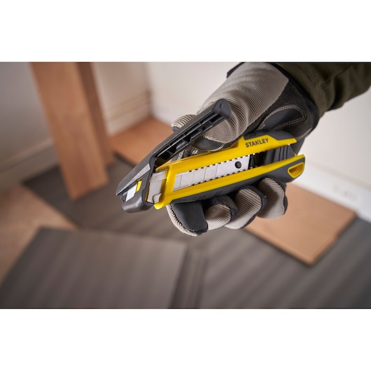 Photo of STANLEY STHT10501-0 utility knife, yellow and black, held in gloved hand, product close-up.