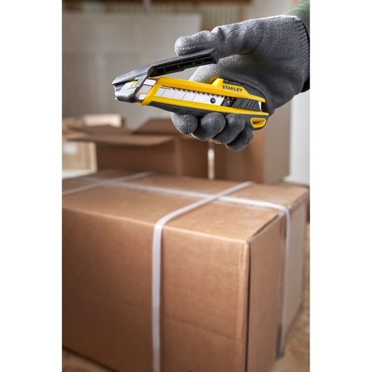 Photo of STANLEY STHT10501-0 utility knife held above cardboard boxes in a warehouse setting.