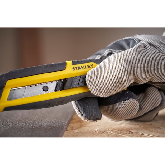 Photo of Stanley STHT10501-0 utility knife in use, yellow and black handle, close-up hand in glove.