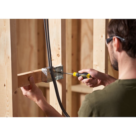 STANLEY STHT16163-0 screwdriver in use tightening a screw in a metal electrical box with wooden studs, close-up.