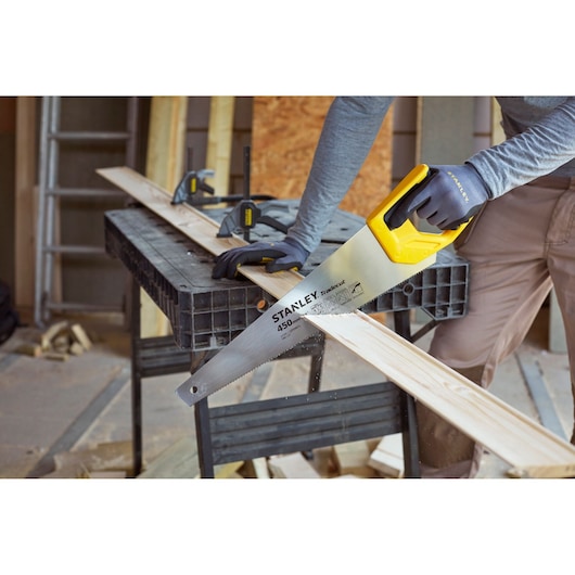 Stanley STHT20355-1 hand saw in use cutting wood, yellow handle, carpentry workspace.